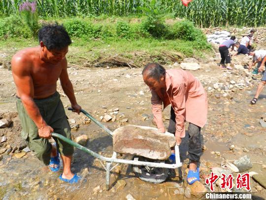 61歲老黨員杜守禮用殘臂扶住小車上的石頭。　張鵬翔 攝